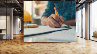 Person writing notes at desk with construction tools. Planning and organizing concepts for work or study in a sunlit workspace. Wall mural