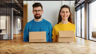 Smiling couple holding cardboard boxes, standing by wall shelves. Concept of moving, packing, and new home lifestyle. Wall mural