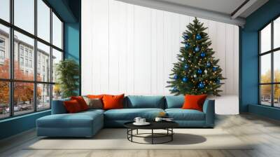 A beautifully decorated Christmas tree with blue ornaments and lights, set against a white wooden wall. The scene is festive and inviting, perfect for holiday celebrations. Wall mural