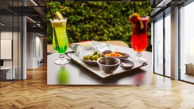 Due cocktail analcolici alla frutta di colore verde e rosso serviti in un bar con snack salati per aperitivo Wall mural