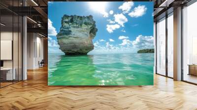 A rock formation in the ocean with a bright blue sky and white clouds. Wall mural