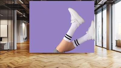 Cropped photo of young school girl legs keeping up with white socks and sneakers on purple background, school uniform concept. Wall mural