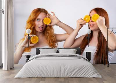 Red-haired girlfriends are having fun and posing with orange slices. Healthy food, spa and beauty, vitamins and happiness concept. Photo on white background Wall mural