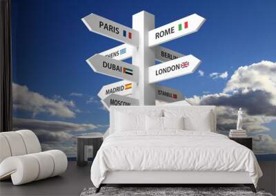 White signpost with various city names on blue sky background Wall mural