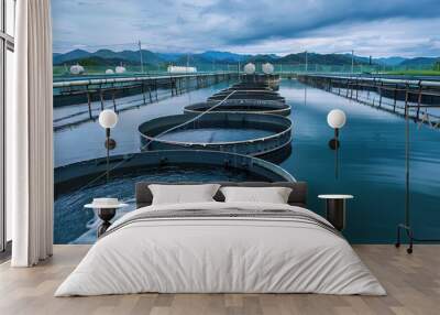 A serene aquaculture facility with circular fish tanks filled with clear water, set against rolling green hills and distant mountains under a dramatic sky. Wall mural