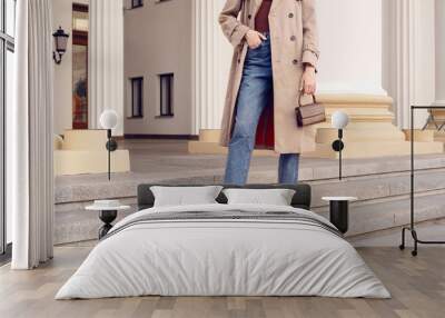 Fashion model woman in beige coat and jeans with brown mini bag on the stairs Wall mural