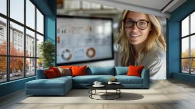 A blonde businesswoman in an office setting, wearing glasses, sitting at the desk, in the office, next to a PC computer. the display shows a AI dashboard. Generative AI. Wall mural