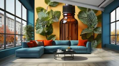 A bottle of essential oil glass is dark amber, a bunch of peppermint leaves nearby, a bright yellow background. Wall mural