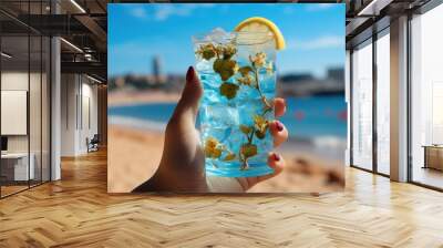 Blue refreshing cocktail at the beach in the woman hand on tropical beach background. Wall mural