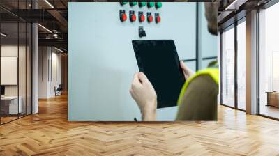 Electrical engineer working on the tablet and recording the voltage current and power of electrical power distribution board in switch gear room Wall mural