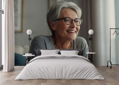 Smiling middle aged mature gray haired woman looking at camera, happy old lady in glasses posing at home indoor, positive single senior retired female sitting on sofa in living room headshot portrait Wall mural