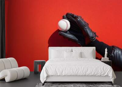 A black baseball glove catches a white baseball on a bright red background. Wall mural