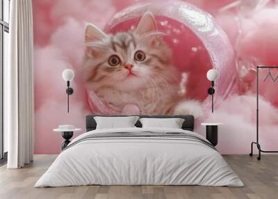 A fluffy grey and white kitten with big brown eyes peeks out from a pink egg-shaped shell, nestled in a bed of pink cotton candy. Wall mural