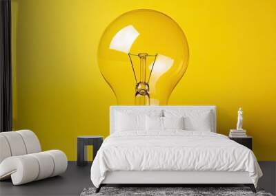 A single, clear light bulb against a bright yellow background, symbolizing ideas, innovation, and creativity. Wall mural