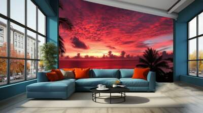 A vibrant red sunset over the ocean with palm trees silhouetted against the sky. Wall mural