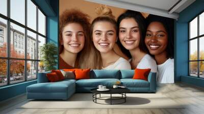 Four diverse young women smiling and looking at the camera with their arms around each other. Wall mural