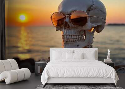 A skeleton wearing sunglasses sitting on a rock by the ocean at sunset Wall mural