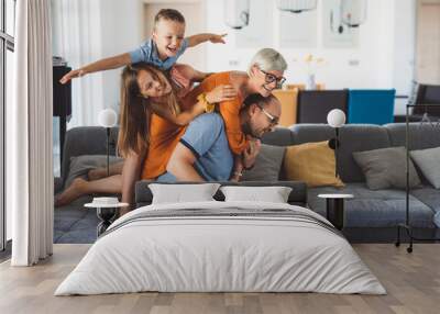 A joyful family of four playing together on a couch in a modern living room. The father is sitting with two children on his back, while the mother smiles at them. The room features stylish decor and n Wall mural