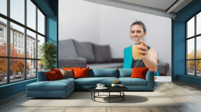 A young woman drinks a vegetable and fruit smoothie in her living room and doing yoga on yoga mat. Wall mural