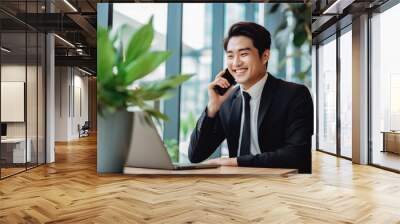 Asian business man smiling and holding cellphone, making a business call. Portrait of confident young man in suit smiling at camera. Business concept Wall mural