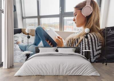 Blonde caucasian female student reading a book while listening to music on headphone Wall mural