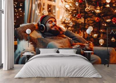 Handsome bearded man in headphones comfortably seated, leaning back, relaxing and listening to good music. Quiet and cozy Christmas celebrations at home Wall mural