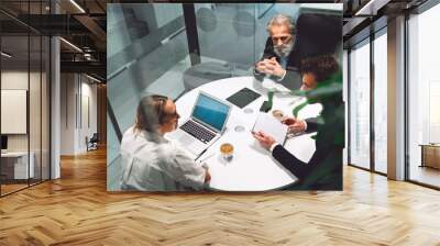 Top down view of three business people sitting by the round table, having a business meeting in a glass office Wall mural