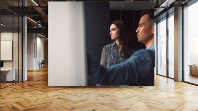 Two business people in business clothes are sitting in an office looking at a contract. One person is giving advice to the other. After signing the contract, they shake hands. Together they look out o Wall mural