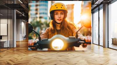 Young woman driving electric scooter in city, wearing yellow helmet. Sunset Wall mural