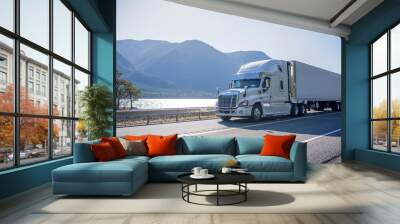 Big rig semi truck with chrome accessories transporting frozen cargo in refrigerated semi trailer moving on the road along river with bewitching view on the opposite bank Wall mural