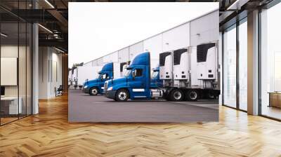 Blue semi trucks and semi trailers stand in row hardly near the warehouse gate under loading and unloading process Wall mural