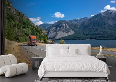 Bright brown big rig semi truck transporting cargo in dry van semi trailer running on the winding highway road along the Columbia River with mountains range on the sides Wall mural