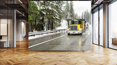 Bright yellow day cab big rig car hauler semi truck with empty semi trailer driving on the winter slippery highway road at snowing time Wall mural