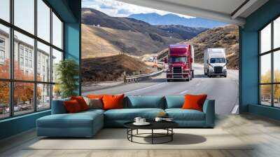 Burgundy and white two different big rig semi trucks with semi trailers climbing uphill on the winding mountain road going to mountain pass in California Wall mural