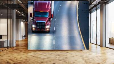 Dark red big rig semi truck transporting cargo in refrigerator semi trailer running on the wide multilines highway at night with turned on headlights Wall mural