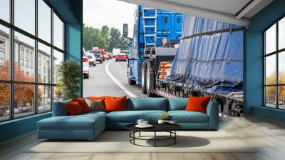 High cab blue big rig long haul semi truck transporting covered and fastened cargo on step down semi trailer driving on the multiline highway road with another traffic Wall mural