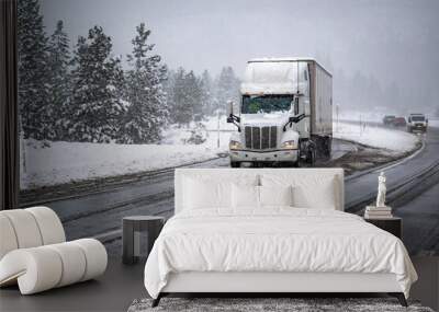 High cab long hauler white big rig semi truck transporting cargo in dry van semi trailer slowly drive on the wet winter highway road with snow and ice at snow storm time Wall mural