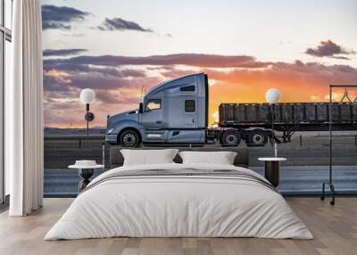 Profile of the gray big rig semi-truck with extended cab transporting boxes on the flat bed semi trailer driving on the flat highway road with sunset sky Wall mural