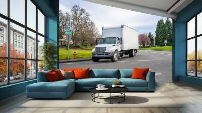 Small compact semi truck with cube box trailer transporting commercial cargo driving on the street of urban city in spring time with blooming trees Wall mural