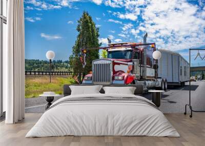 Specially equipped big rig classic red semi truck with oversize load sign transporting manufactory house on step down semi trailer running on the road with escort car Wall mural