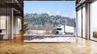 White big rig long haul semi truck with refrigerator semi trailer running on the winding winter snowy road with forest Wall mural