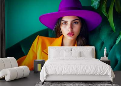 Beautiful cheeky confident Mexican young woman in yellow business suit with purple hat sits at a table indoors. Fashionable brunette girl. Direct look Wall mural