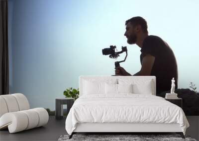 A young man sits on a stone with a camera in his hands. Man shoots at camera nature. Wall mural