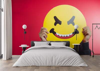 A person is holding a yellow smiley face in front of their face Wall mural