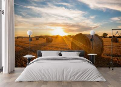 Beautiful bright sun rays under horizon over the field after harvesting. Straw bales outdoors on warm sunny summer evening. Wall mural