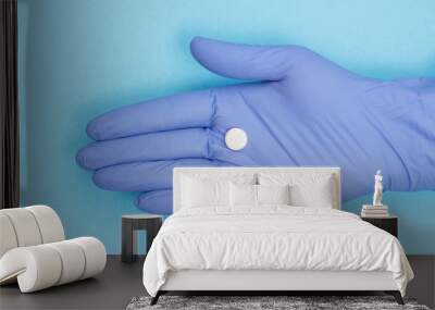 Female doctor in blue glove with white pill on the palm of her hand. Wall mural