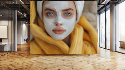 Close-up of a woman with a white facial mask and a yellow robe, highlighting her blue eyes and relaxed expression. Wall mural