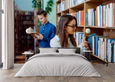 Students in the library searching for materials to make a group project. Young girl and boy working on their homework after classes. Wall mural