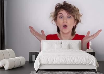 Close- up portrait of a young rather surprised woman with an open mouth standing with open hands, isolated on a grey background Wall mural