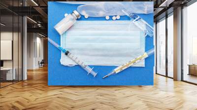 medical protective masks with thermometer, syringe, ampoule, medicine bottle, pills on a blue background with copy space. Wall mural